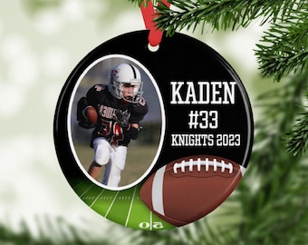 May include: A black and white round Christmas ornament with a photo of a football player. The ornament has the name "KADEN", the number "#33", and "KNIGHTS 2023" printed on it. A brown football graphic is also included.