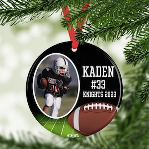 May include: A black and white round Christmas ornament with a photo of a football player. The ornament has the name "KADEN", the number "#33", and "KNIGHTS 2023" printed on it. A brown football graphic is also included.