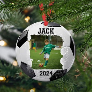 May include: A white and black soccer ball Christmas ornament with a photo of a child playing soccer. The ornament has the name "JACK" and the year "2024" printed on it.