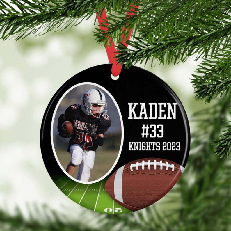 May include: A black and white round Christmas ornament with a photo of a football player. The ornament has the name "KADEN", the number "#33", and "KNIGHTS 2023" printed on it. A brown football graphic is also included.