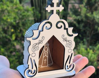 May include: A white and black wooden religious shrine with a cross on top. The shrine features an arched doorway with a religious figure inside. The design includes decorative swirls and a base.