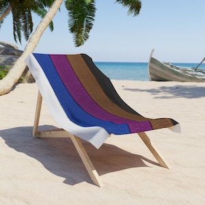 May include: A beach chair with a white, blue, purple, brown, and black striped beach towel. The chair is made of wood and has a white fabric seat.