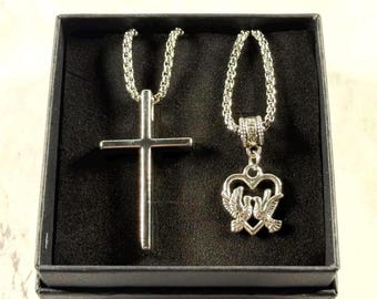 Two necklace set with a crucifix pendant and a doves-with-heart pendant beside a gift box