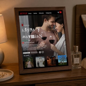 Puede incluir: Un marco de madera rectangular que muestra una pantalla digital con una interfaz de Netflix. La pantalla presenta el título de película Keyla y Mathias, una pareja con copas de vino, menús de navegación, una sinopsis y varias miniaturas.