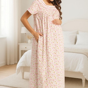 Puede incluir: Camisón largo con estampado floral en una suave paleta de colores rosa y crema. El camisón presenta mangas cortas, un escote redondo y bolsillos. La tela está cubierta de pequeños estampados florales rosas y dorados. La mujer está en un dormitorio.