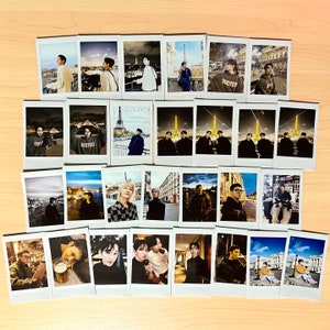 May include: A collection of 27 Polaroid photos featuring various people in different settings. Some photos show people in Paris, France, while others show people in different locations. The photos are arranged in a grid pattern on a wooden surface.