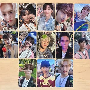 May include: A collection of eleven photo cards featuring various individuals. Each card displays a different person, with diverse hairstyles and clothing. The cards are arranged on a light-colored wooden surface, creating a visually appealing display.