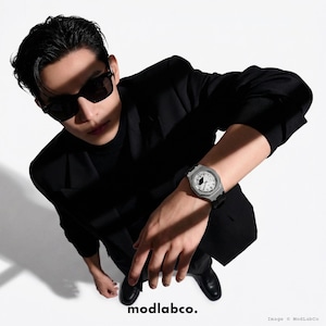May include: A silver wristwatch with a white face and black hands is displayed. The watch has a black band and is worn on a wrist. The image also shows a person wearing sunglasses and a black suit. The text "modlabco." is at the bottom.