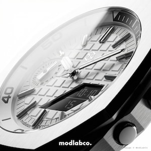May include: Close-up of a modern silver wristwatch with a black band. The watch face features a digital display showing the time, along with analog hands and markers. The watch has a textured dial and the brand name "modlabco." is visible.