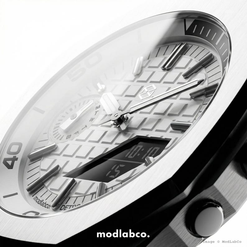 May include: Close-up of a modern silver wristwatch with a black band. The watch face features a digital display showing the time, along with analog hands and markers. The watch has a textured dial and the brand name "modlabco." is visible.