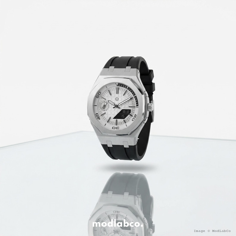 May include: A silver-toned wristwatch with a white face and black rubber band. The watch features a digital display and analog dials. The watch is displayed on a reflective surface.