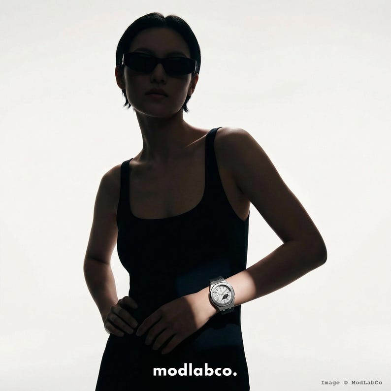 May include: A person wearing a black tank top and sunglasses, with a silver wristwatch. The watch has a round face and a silver band. The image includes the text "modlabco."