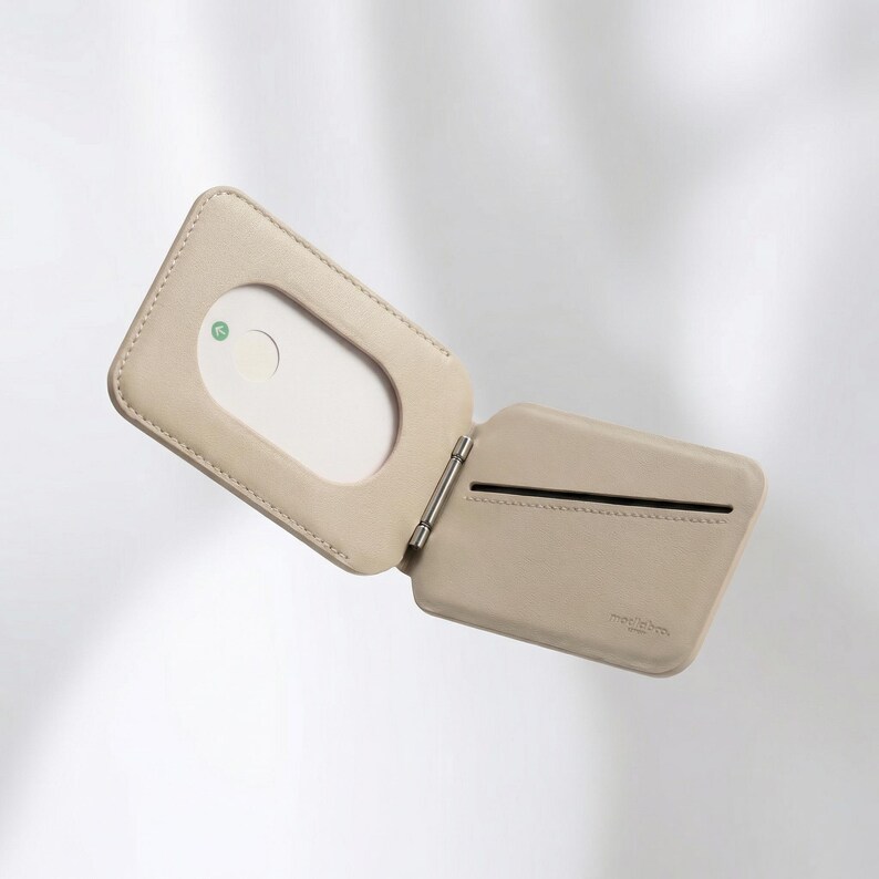 Puede incluir: Cartera de cuero beige claro abierta, con una ventana rectangular y una ranura para tarjetas. La cartera est&aacute; articulada con una bisagra de metal plateado. El interior presenta una tarjeta blanca con un dise&ntilde;o circular verde y blanco.