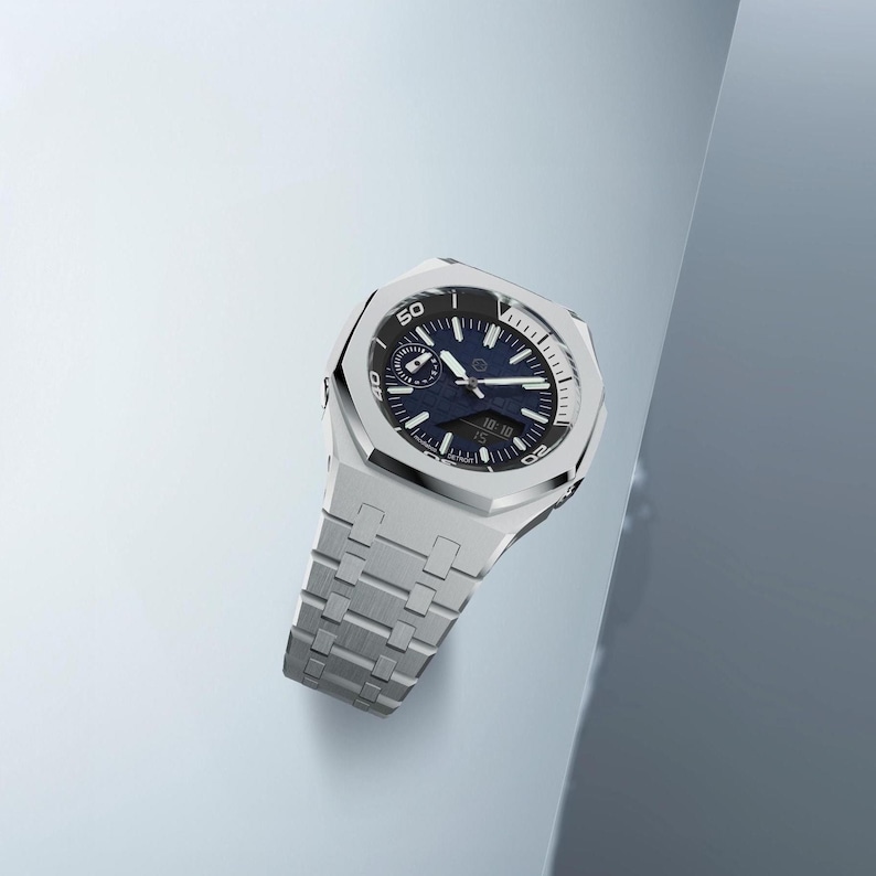 May include: A silver-toned wristwatch with a blue face and a matching silver band. The watch has a round dial with white markings and a rotating bezel. The watch displays the time as 10:10. The watch is a luxury item.