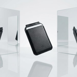 Peut inclure: Une housse de t&eacute;l&eacute;phone en cuir noir avec une fente pour carte. La housse rectangulaire a un dessus arrondi et un petit logo en relief. Le fond est blanc avec des reflets de la housse.