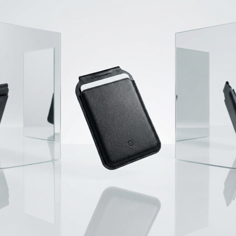Peut inclure: Une housse de t&eacute;l&eacute;phone en cuir noir avec une fente pour carte. La housse rectangulaire a un dessus arrondi et un petit logo en relief. Le fond est blanc avec des reflets de la housse.