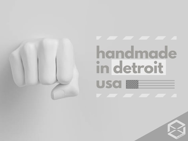 May include: A grayscale image featuring a clenched fist sculpture. The text "handmade in detroit usa" is displayed with an American flag graphic. The overall design is minimalist and modern, with a focus on the fist.