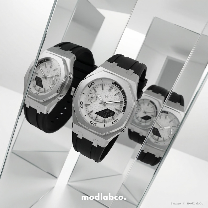 May include: Two silver watches with black bands are displayed in front of a mirrored surface. The watches have white faces with black numbers and hands. The watches are angled towards the viewer, showcasing their design. The image is well-lit, highlighting the watches' details.