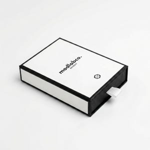 May include: A rectangular black and white box with the text "modlabco. DETROIT" and a small geometric symbol. The box has a white lid and a black base, with a white ribbon pull.