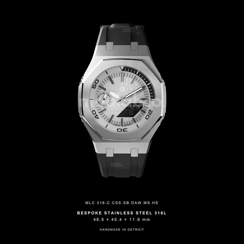 May include: A stainless steel watch with a white face and black accents. The watch has a rectangular shape with a black band. The watch face displays the time and date. The watch measures 48.5 x 45.4 x 11.9 mm. Text on the watch reads "HANDMADE IN DETROIT".