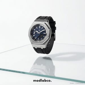 Op de afbeelding: Een roestvrijstalen horloge met een blauwe wijzerplaat en een zwarte rubberen band. Het horloge heeft een ronde wijzerplaat met witte markeringen en een datumweergave. Het horloge wordt op een transparant oppervlak weergegeven.
