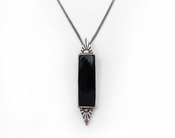 Può includere: Una collana con catena d'argento con un ciondolo rettangolare nero. Il ciondolo ha un design a raggiera d'argento in alto e in basso.