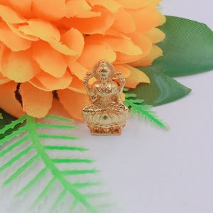 May include: A gold-colored Lakshmi deity figurine sitting on a lotus flower. The figurine is wearing a crown and jewelry and has four arms.