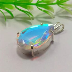 Op de afbeelding: Een parelmoerachtige, regenboogkleurige edelsteen hanger in een zilveren setting. De edelsteen heeft een traanvorm en toont een regenboogkleuren.