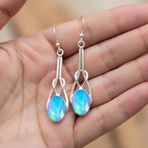 May include: Silver drop earrings with oval, faceted, iridescent blue opal stones. The earrings have a distinctive looped design above the opals and a simple hook closure. The opals display a range of blue and green hues. The earrings are a beautiful accessory.