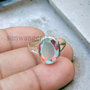 May include: A silver ring with a large oval-shaped gemstone. The gemstone is a light blue color with red and orange flashes of color.