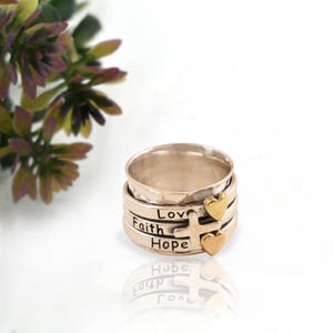 May include: A silver spinning ring with four bands. The bands are engraved with the words "Love", "Faith", "Hope", and a cross. The ring has two gold heart charms.
