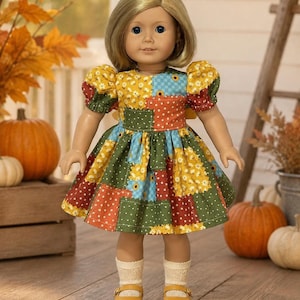 May include: A doll with blonde hair and blue eyes wearing a patchwork dress featuring floral and checkered patterns in yellow, green, blue, and red. The doll has short puffed sleeves, cream-colored socks, and yellow buckled shoes on its feet.