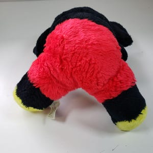 May include: A red and black plush toy with yellow accents. The toy is shaped like a cartoon character and has a fluffy texture.