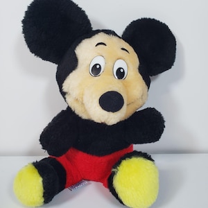 Pode incluir: Um brinquedo de pel&uacute;cia do Mickey Mouse com pelo preto, shorts vermelhos e sapatos amarelos. O brinquedo tem um grande sorriso e olhos grandes.