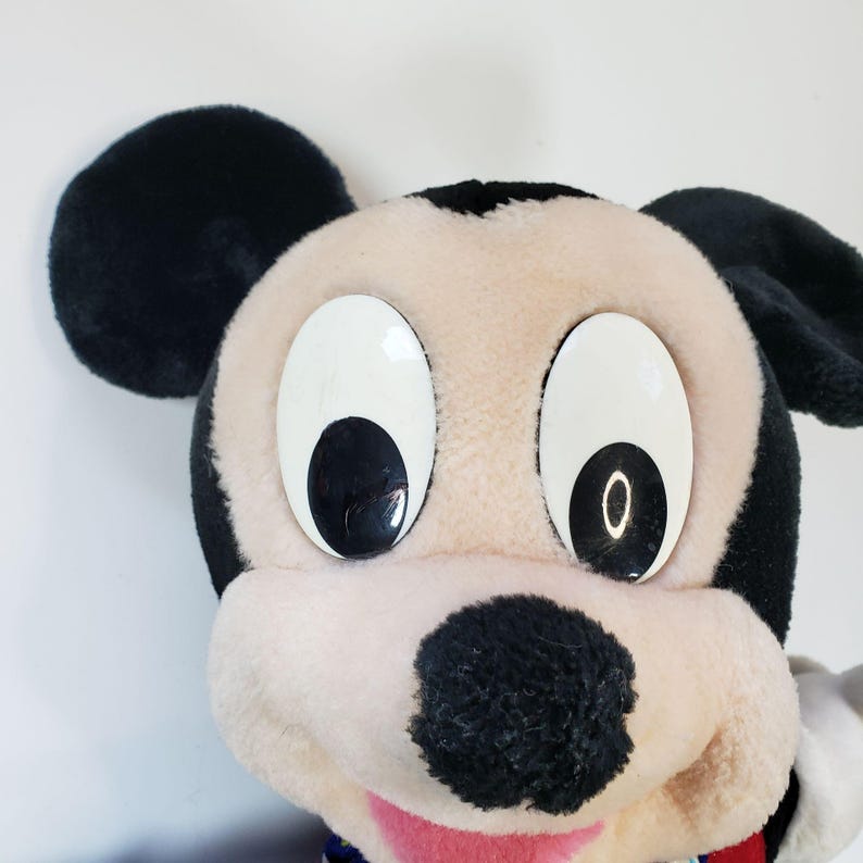 K&ouml;nnte beinhalten: Nahaufnahme eines Pl&uuml;sch-Mickey-Mouse-Spielzeugs mit schwarzen Ohren, einer schwarzen Nase und gro&szlig;en wei&szlig;en Augen mit schwarzen Pupillen. Das Spielzeug hat einen rosa Mund und ist aus weichem, pl&uuml;schigen Stoff.