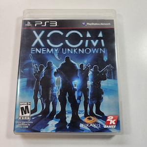 May include: A PlayStation 3 game case for XCOM: Enemy Unknown. The cover features a blue-toned image of soldiers with weapons, the game's title, and the PlayStation 3 and ESRB logos. The case is in a clear plastic sleeve.