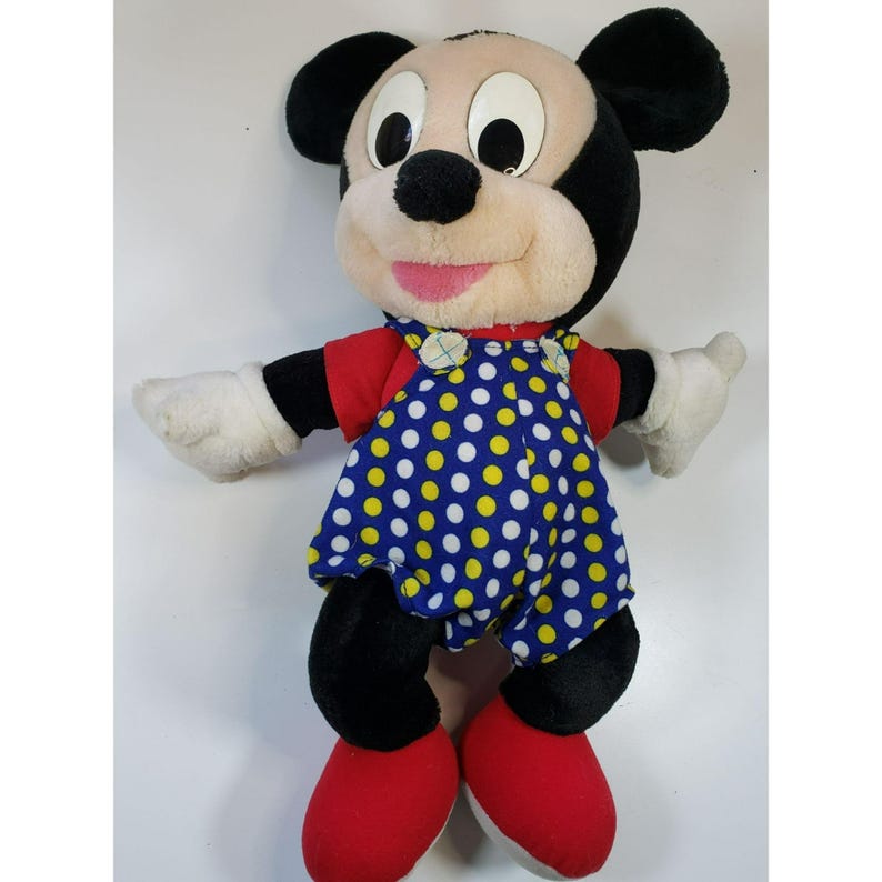 K&ouml;nnte beinhalten: Ein Pl&uuml;sch-Mickey-Mouse-Spielzeug, das ein blaues und gelbes gepunktetes Kleid mit roten Schuhen tr&auml;gt.