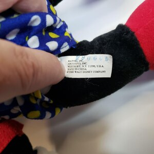 K&ouml;nnte beinhalten: Ein schwarzes, rotes und blaues Pl&uuml;schtier mit einem wei&szlig;en Tupfenmuster. Das Spielzeug hat ein Etikett mit der Aufschrift "MATTEL, INC. ARCOTOYS, INC. WESTBURY, N.Y. 11590, U.S.A. MADE IN CHINA &copy; THE WALT DISNEY COMPANY."