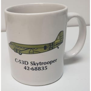 May include: White ceramic mug with a green and brown illustration of a C-53D Skytrooper airplane with the text "C-53D Skytrooper 42-68835" printed on the front.
