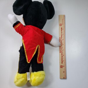 May include: A plush Mickey Mouse toy wearing a red and gold tuxedo. The toy is approximately 12 inches tall and has black ears, yellow shoes, and a white face.