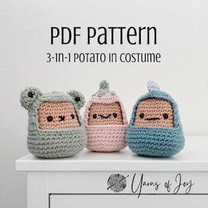 May include: Three crocheted potato toys wearing different costumes: a green frog, a pink unicorn, and a blue dinosaur. The toys are sitting on a white surface with the text "PDF pattern 3-in-1 potato in costume" above them and "Yarns of Joy" below them.