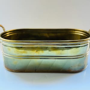 May include: A brass planter with two handles. The planter is oval shaped and has a shiny finish.