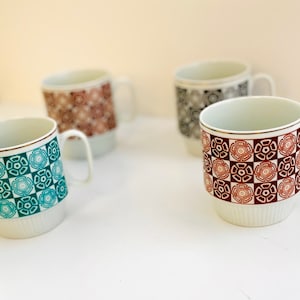 Può includere: Quattro tazze in ceramica con diversi motivi geometrici. Le tazze sono bianche con disegni marroni, turchese e neri.