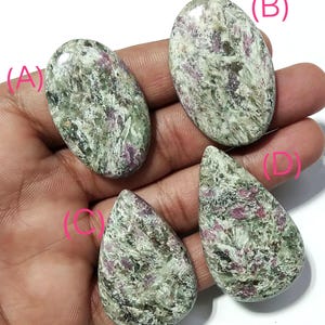 以下が含まれることがあります： 緑、白、ピンクの色合いが混ざった、研磨された4つの宝石。2つは楕円形で、2つは涙の形をしています。石はマーブル模様で、色と質感が混ざっています。宝石は手で持たれています。