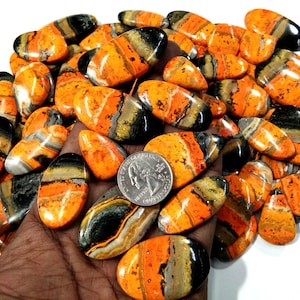 以下が含まれることがあります： 黒、オレンジ、白の縞模様が特徴的な、研磨された楕円形の天然石のコレクション。石は約2.5cmの長さで、手に置かれています。