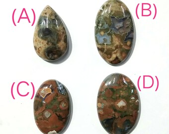 May include: Four polished gemstone cabochons in various shapes. The stones display a mix of colors, including brown, green, and beige, with unique patterns. The cabochons are labeled A, B, C, and D.