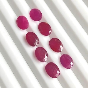 Peut inclure: Une sélection de pierres précieuses ovales, rouge foncé, disposées sur une surface blanche. Les gemmes sont polies et facettées, reflétant la lumière. L'arrangement met en valeur la couleur et la forme des pierres, pour la création de bijoux.