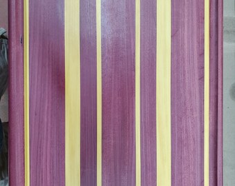 May include: A large, rectangular cutting board made of wood with alternating stripes of purple and yellow wood. The board has a raised edge around the perimeter.