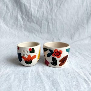 May include: Two ceramic cups with floral designs. One cup has the word "boho" written on it.