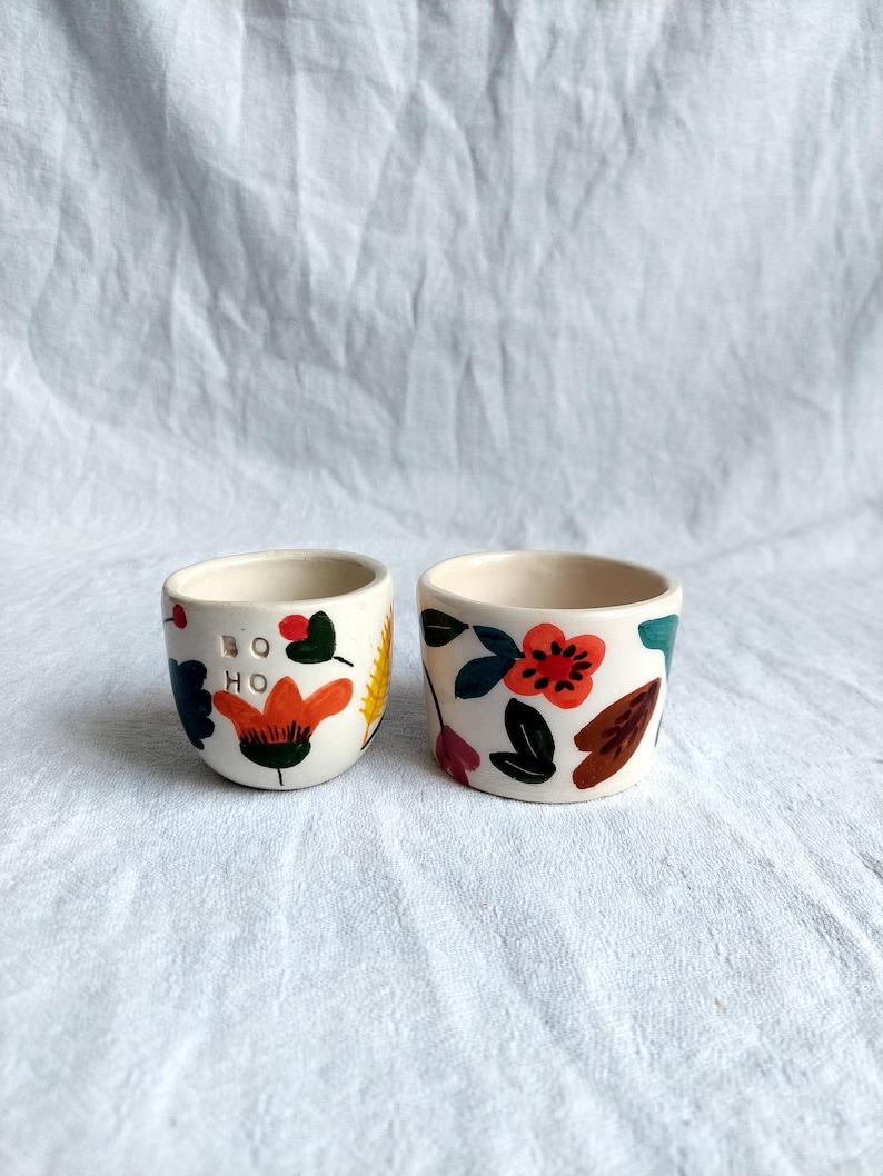 May include: Two ceramic cups with floral designs. One cup has the word "boho" written on it.